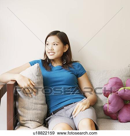 Stock Photo - Young woman sitting on a couch and smiling. Fotosearch