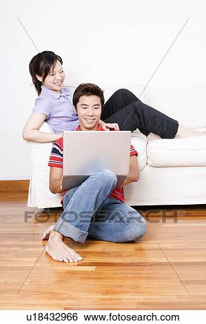 Young woman sitting on a couch with a mid adult man using a laptop View Large Photo Image Stock Photograph - Young woman sitting on a couch with a mid adult man using a laptop. Fotosearch