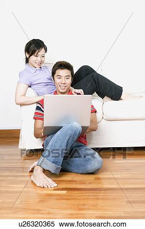 Young woman sitting on a couch with a mid adult man using a laptop View Large Photo Image Stock Photography - Young woman sitting on a couch with a mid adult man using a laptop. Fotosearch
