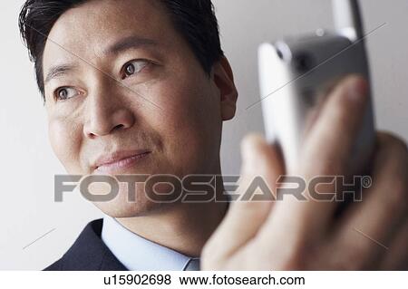 Stock Photo - Close-up of a businessman holding a mobile phone thinking. Fotosearch