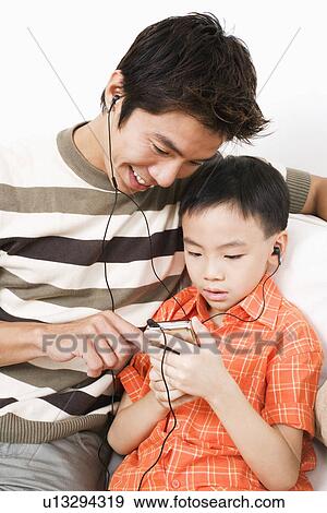 Close-up of a mid adult man and his son listening to an MP3 player View Large Photo Image Stock Photo - Close-up of a mid adult man and his son listening to an MP3 player. Fotosearch