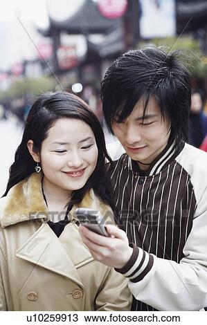 Stock Image - Close-up of a young couple looking at a mobile phone smiling. Fotosearch