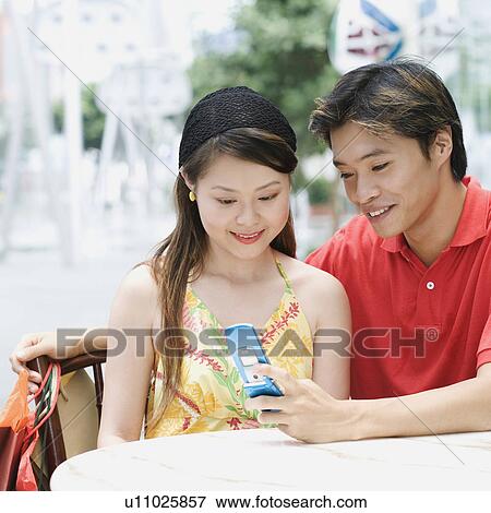 Close-up of a young couple sitting in a cafeteria and looking at mobile phone View Large Photo Image Stock Photo - Close-up of a young couple sitting in a cafeteria and looking at mobile phone. Fotosearch