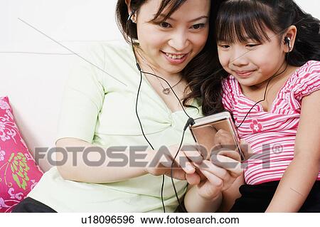 Close-up of a young woman and her daughter listening to an MP3 player View Large Photo Image Stock Photograph - Close-up of a young woman and her daughter listening to an MP3 player. Fotosearch
