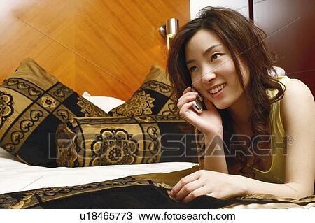 Close-up of a young woman lying on the bed using a mobile phone View Large Photo Image Stock Image - Close-up of a young woman lying on the bed using a mobile phone. Fotosearch
