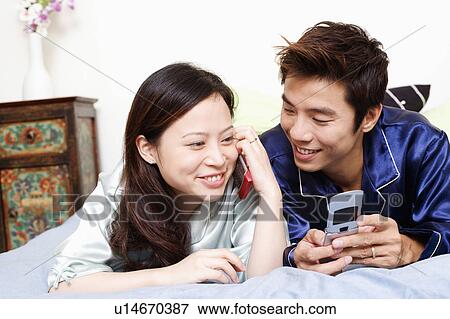 Close-up of a young woman talking on mobile phone with a mid adult man lying beside her View Large Photo Image Stock Photo - Close-up of a young woman talking on mobile phone with a mid adult man lying beside her. Fotosearch