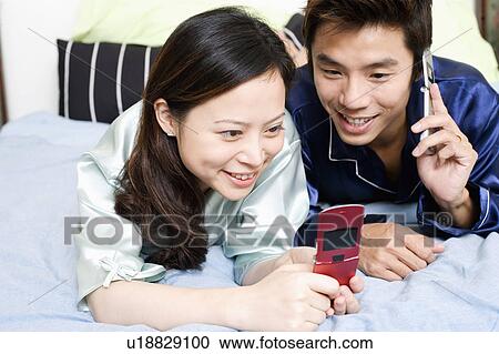 Close-up of a young woman using a mobile phone with a mid adult man lying beside her View Large Photo Image Stock Image - Close-up of a young woman using a mobile phone with a mid adult man lying beside her. Fotosearch