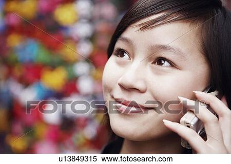 Close-up of a young woman using a mobile phone looking away View Large Photo Image Stock Photography - Close-up of a young woman using a mobile phone looking away. Fotosearch