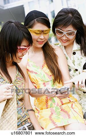 Stock Image - Close-up of three young women looking at a mobile phone. Fotosearch
