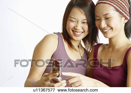 Stock Photo - Close-up of two young women looking at a mobile phone and smiling. Fotosearch