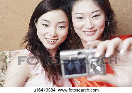 Picture - Close-up of two young women taking a photograph of themselves. Fotosearch