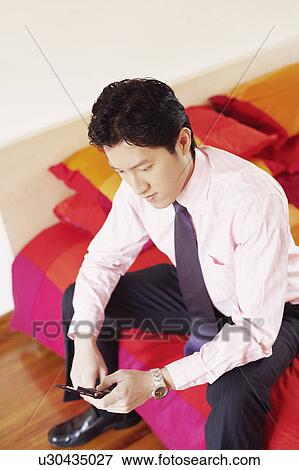 High angle view of a businessman sitting on the bed and operating a mobile phone View Large Photo Image Stock Photo - High angle view of a businessman sitting on the bed and operating a mobile phone. Fotosearch
