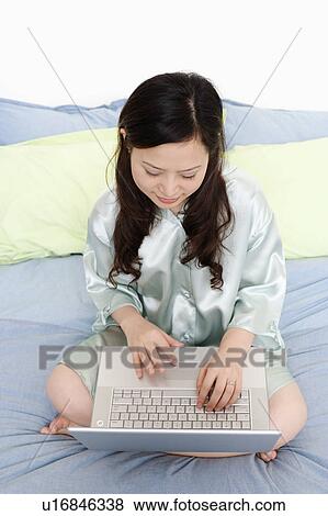 High angle view of a young woman using a laptop on the bed View Large Photo Image Stock Photo - High angle view of a young woman using a laptop on the bed. Fotosearch