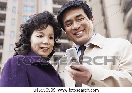 Low angle view of a mature couple looking at a mobile phone smiling View Large Photo Image Stock Photo - Low angle view of a mature couple looking at a mobile phone smiling. Fotosearch