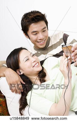 Mid adult man and a young woman lying on a couch and listening to an MP3 player View Large Photo Image Stock Photo - Mid adult man and a young woman lying on a couch and listening to an MP3 player. Fotosearch
