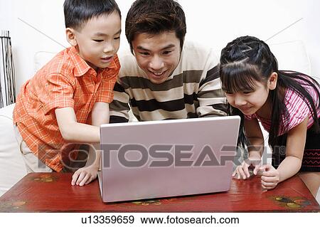 Mid adult man using a laptop with his son and daughter beside him View Large Photo Image Stock Photo - Mid adult man using a laptop with his son and daughter beside him. Fotosearch