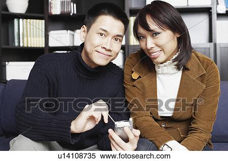 Portrait of a young man sitting with a young woman on a couch holding a mobile phone View Large Photo Image Stock Photography - Portrait of a young man sitting with a young woman on a couch holding a mobile phone. Fotosearch