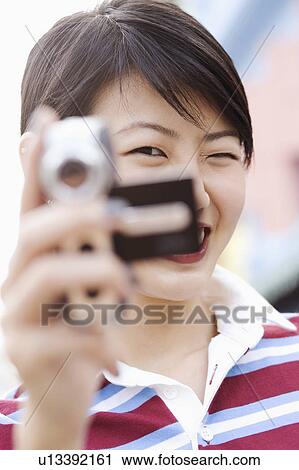 Stock Image - Portrait of a young woman holding a digital camera. Fotosearch