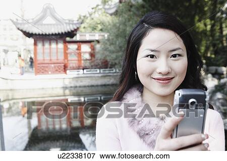 Portrait of a young woman holding a mobile phone smiling View Large Photo Image Stock Photo - Portrait of a young woman holding a mobile phone smiling. Fotosearch