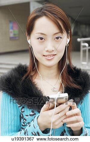 Stock Photo - Portrait of a young woman listening to an MP3 player. Fotosearch