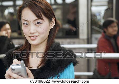 Stock Image - Portrait of a young woman operating a mobile phone with a digitized pen. Fotosearch