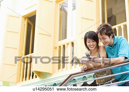 Young couple leaning against a railing and looking at a mobile phone View Large Photo Image Stock Image - Young couple leaning against a railing and looking at a mobile phone. Fotosearch