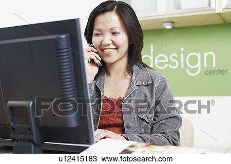 Close-up of a businesswoman sitting in front of a computer using a mobile phone View Large Photo Image Stock Image - Close-up of a businesswoman sitting in front of a computer using a mobile phone. Fotosearch