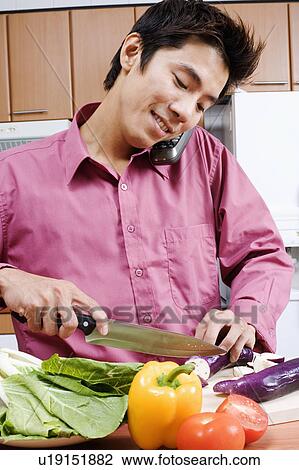 Close-up of a mid adult man cutting vegetables while talking on a cordless phone View Large Photo Image Stock Image - Close-up of a mid adult man cutting vegetables while talking on a cordless phone. Fotosearch
