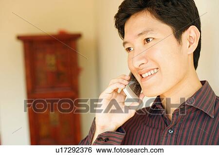 Close-up of a young man smiling and talking on a mobile phone View Large Photo Image Stock Photograph - Close-up of a young man smiling and talking on a mobile phone. Fotosearch