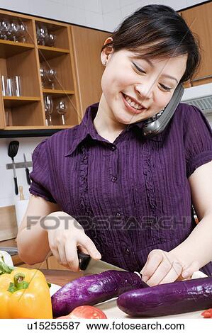 Stock Photo - Close-up of a young woman cutting vegetables and talking on a cordless phone. Fotosearch