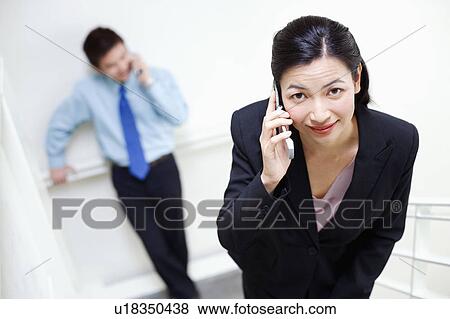 Portrait of a businesswoman talking on a mobile phone with a businessman standing behind her View Large Photo Image Stock Photo - Portrait of a businesswoman talking on a mobile phone with a businessman standing behind her. Fotosearch