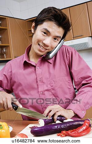 Portrait of a mid adult man cutting vegetables while talking on a cordless phone View Large Photo Image Picture - Portrait of a mid adult man cutting vegetables while talking on a cordless phone. Fotosearch