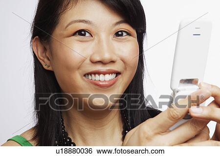 Portrait of a young woman smiling and operating a mobile phone View Large Photo Image Stock Photograph - Portrait of a young woman smiling and operating a mobile phone. Fotosearch