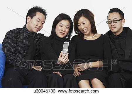 Two young men and two young women sitting on a couch looking at a mobile phone View Large Photo Image Stock Image - Two young men and two young women sitting on a couch looking at a mobile phone. Fotosearch