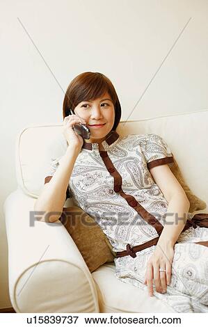 Stock Photo - Young woman sitting on a couch and talking on a mobile phone. Fotosearch