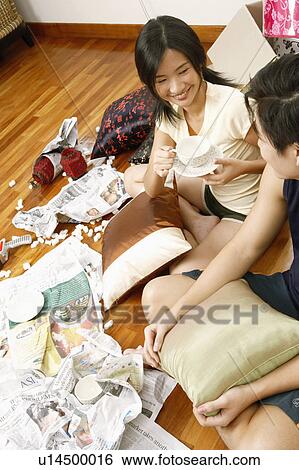 Stock Photograph - High angle view of a young woman sitting on the floor with a young man and holding a cup. Fotosearch
