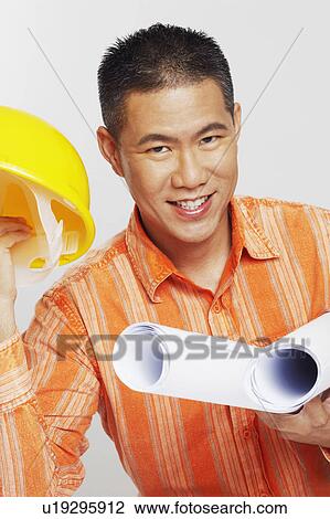 Stock Image - Portrait of a male architect holding two blueprints and a hardhat. Fotosearch