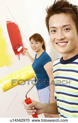 Stock Image - Portrait of a young man holding a paint roller with a young woman standing in the background. Fotosearch