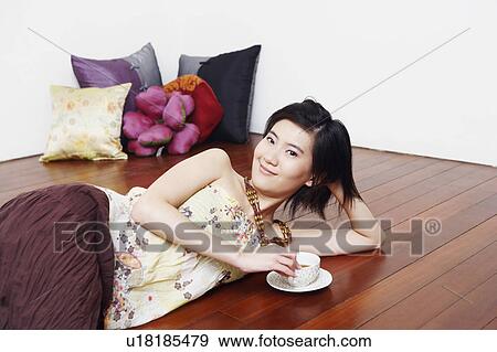Stock Photo - Portrait of a young woman lying on the floor and holding a cup of tea. Fotosearch