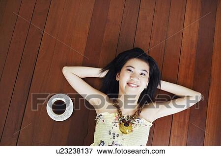 Portrait of a young woman lying on the floor with her hands behind her head View Large Photo Image Stock Photo - Portrait of a young woman lying on the floor with her hands behind her head. Fotosearch