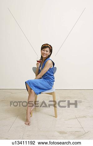 Portrait of a young woman sitting on a chair and holding a glass of wine View Large Photo Image Stock Image - Portrait of a young woman sitting on a chair and holding a glass of wine. Fotosearch