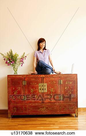 Portrait of a young woman sitting on a cabinet with a laptop beside her View Large Photo Image Stock Photo - Portrait of a young woman sitting on a cabinet with a laptop beside her. Fotosearch