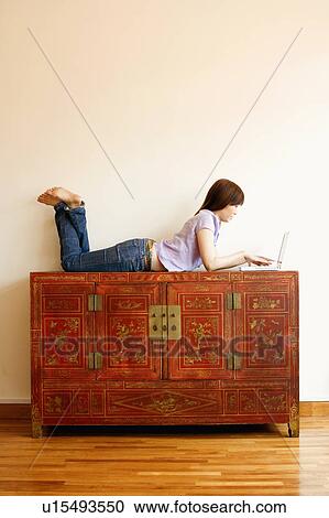 Stock Image - Side profile of a young woman lying on a trunk and working on a laptop. Fotosearch