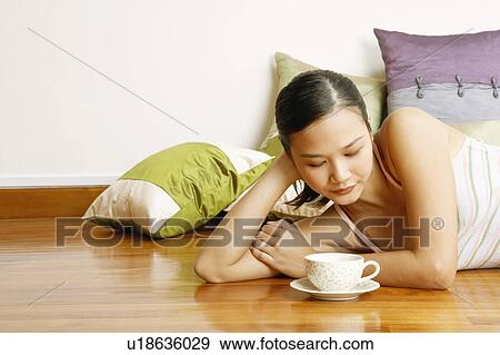 Young woman lying on the floor and looking at a tea cup View Large Photo Image Stock Photo - Young woman lying on the floor and looking at a tea cup. Fotosearch