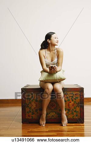 Young woman sitting on a trunk and listening to music View Large Photo Image Stock Photograph - Young woman sitting on a trunk and listening to music. Fotosearch