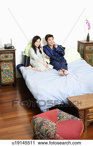 Stock Image - High angle view of a mid adult man using a telephone with a young woman talking on mobile phone. Fotosearch
