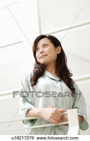 Stock Photo - Low angle view of a young woman standing beside a railing. Fotosearch