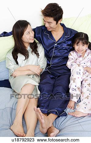 Stock Image - Portrait of a girl sitting with her parents on the bed. Fotosearch