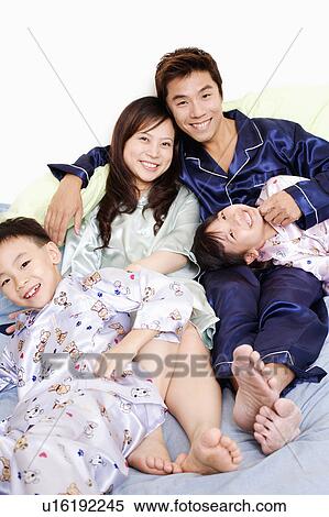 Stock Photography - Portrait of a mid adult man and a young woman smiling with their children on the bed. Fotosearch
