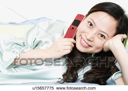 Portrait of a young woman holding a mobile phone and smiling View Large Photo Image Stock Photography - Portrait of a young woman holding a mobile phone and smiling. Fotosearch